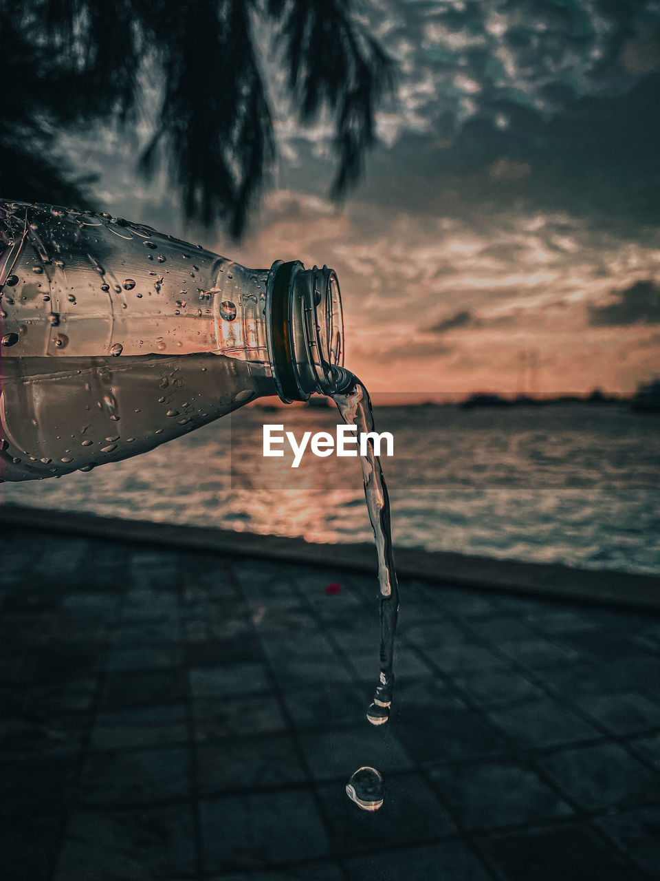 Close-up of water drops on glass against sea at sunset