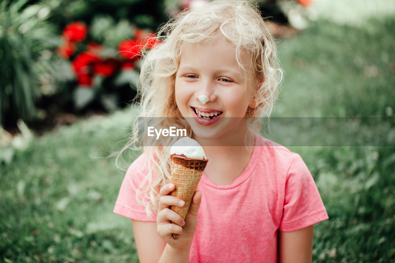  funny adorable girl with dirty nose and milk moustaches eating licking ice cream from waffle cone. 