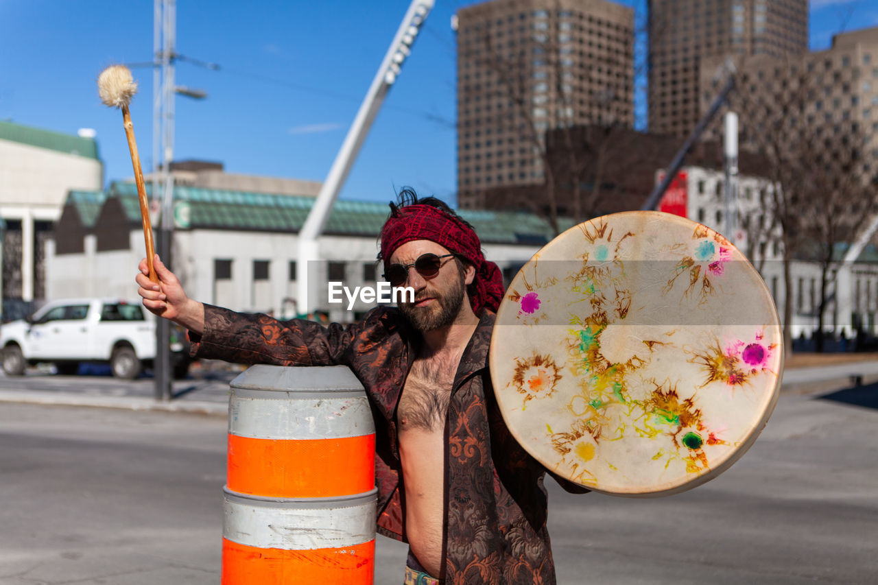 Portrait of man holding drum while standing at city