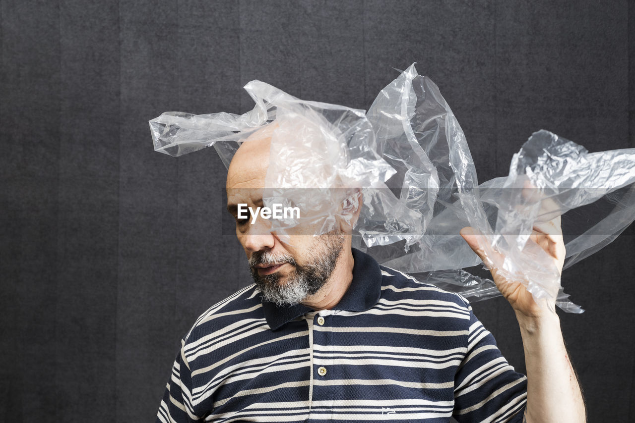 Mature man with a transparent plastic bag flying over his head and face. 