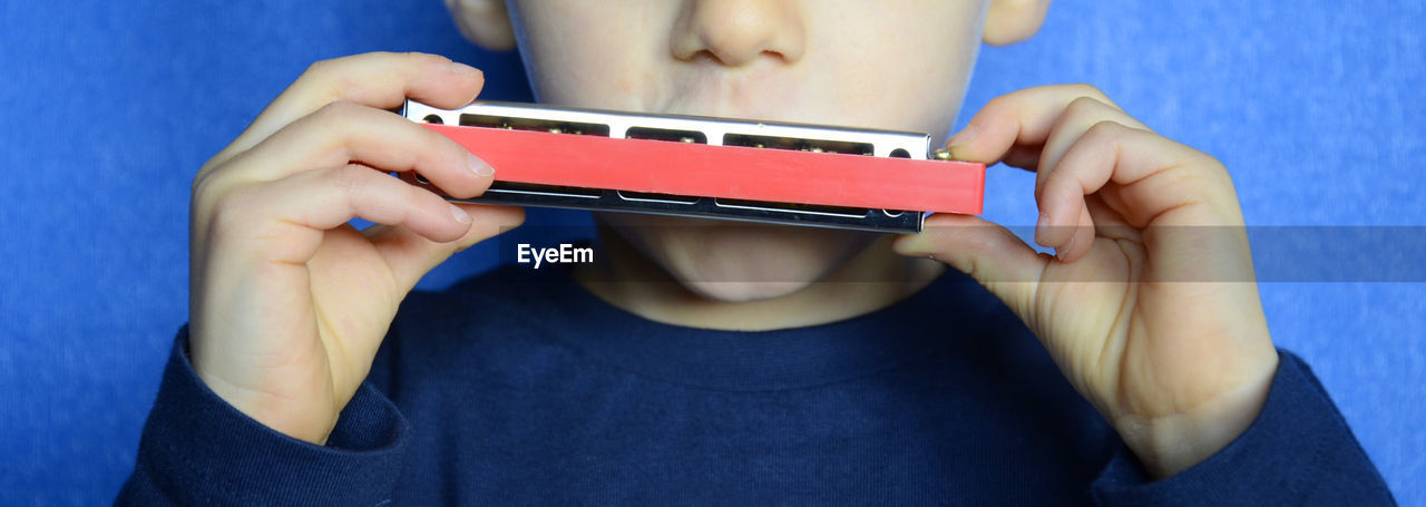 Midsection of boy playing harmonica against wall