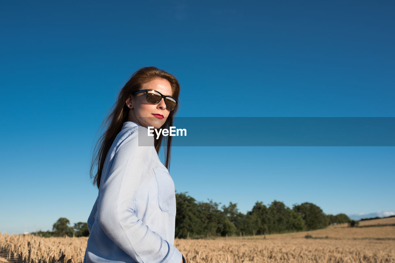 Portrait of beautiful young woman standing on wheat field against clear sky