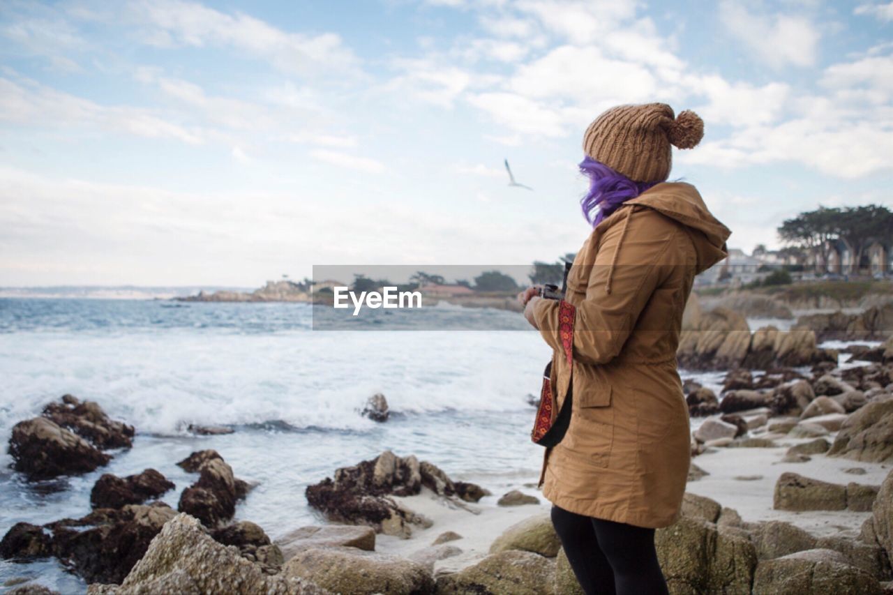 Side view of woman standing at rocky shore against sky during winter