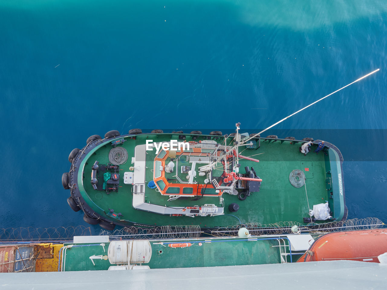 Tug boat approaching to the container vessel for mooring near the port. view from above.