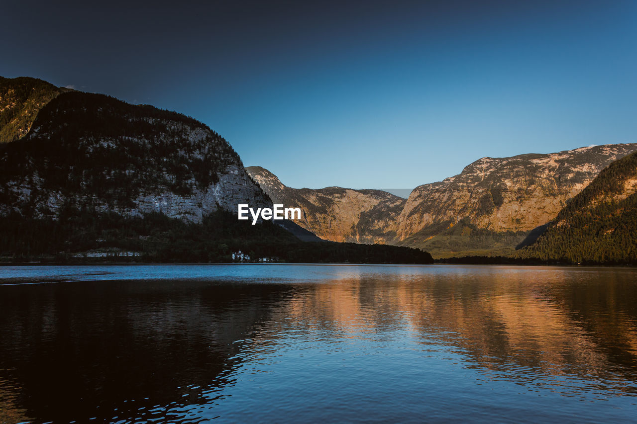 Scenic view of lake and mountains against clear blue sky