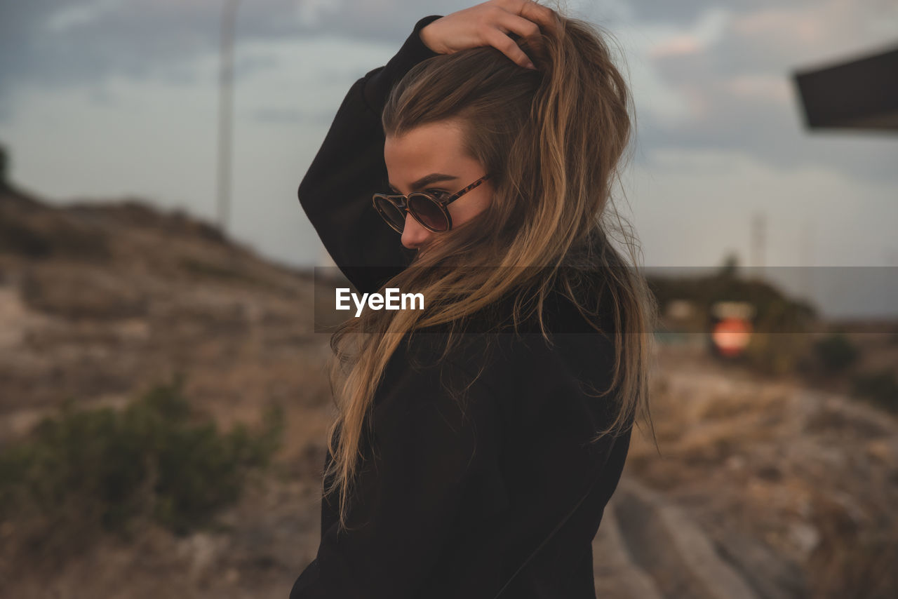 Young woman wearing sunglasses against sky during sunset