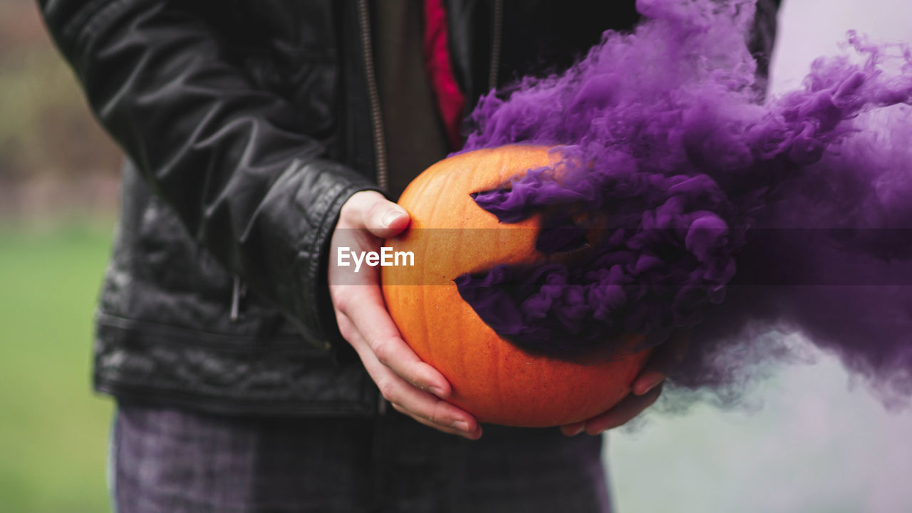 Midsection of man holding smoke emitting jack o lantern outdoors