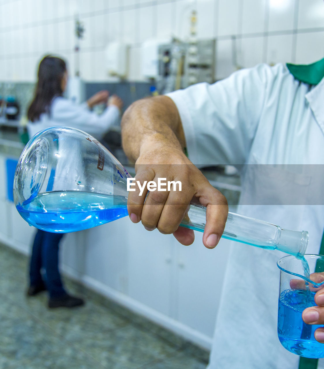 Midsection of scientist pouring liquid in beaker at laboratory