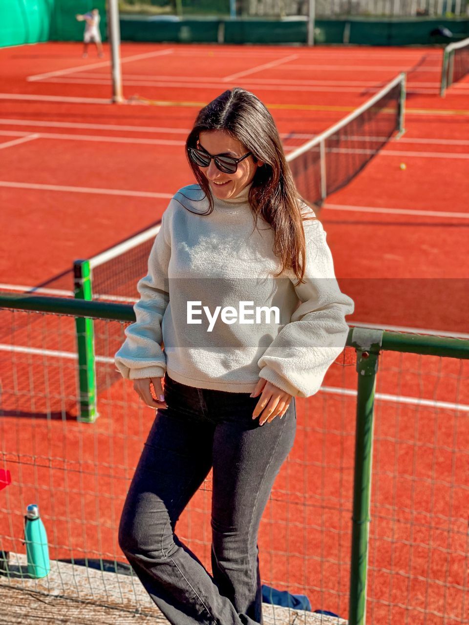 one person, young adult, glasses, adult, women, sports, lifestyles, full length, red, track and field event, front view, hairstyle, sunglasses, clothing, fashion, standing, day, jumping, casual clothing, long hair, portrait, smiling, footwear, sport venue, athlete, eyeglasses, happiness, emotion, leisure activity, looking at camera, outdoors, trousers, looking, sunlight, brown hair, female, person, running track