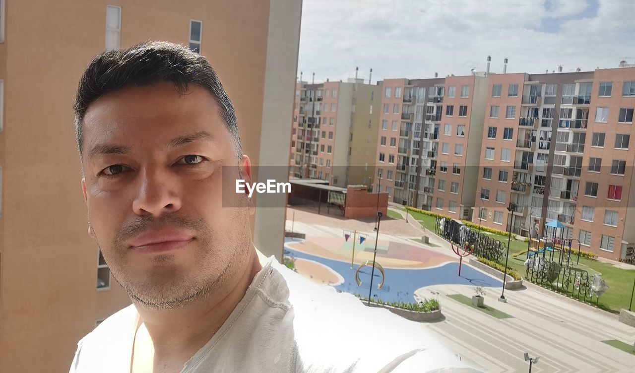 portrait, one person, architecture, headshot, adult, building exterior, men, city, built structure, looking at camera, young adult, building, front view, person, day, lifestyles, nature, beard, window, serious, outdoors, looking, apartment