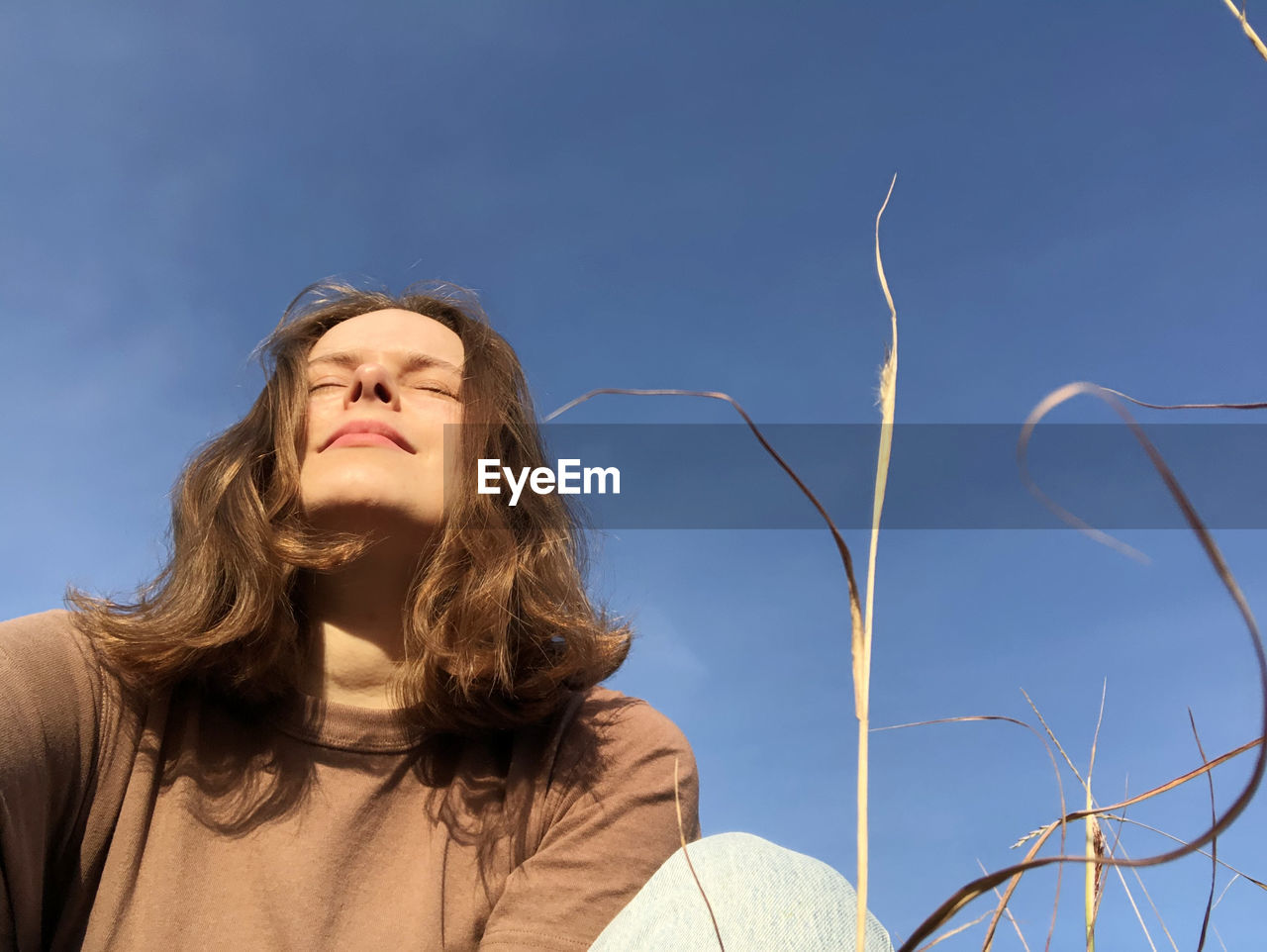 Low angle portrait of woman standing against blue sky