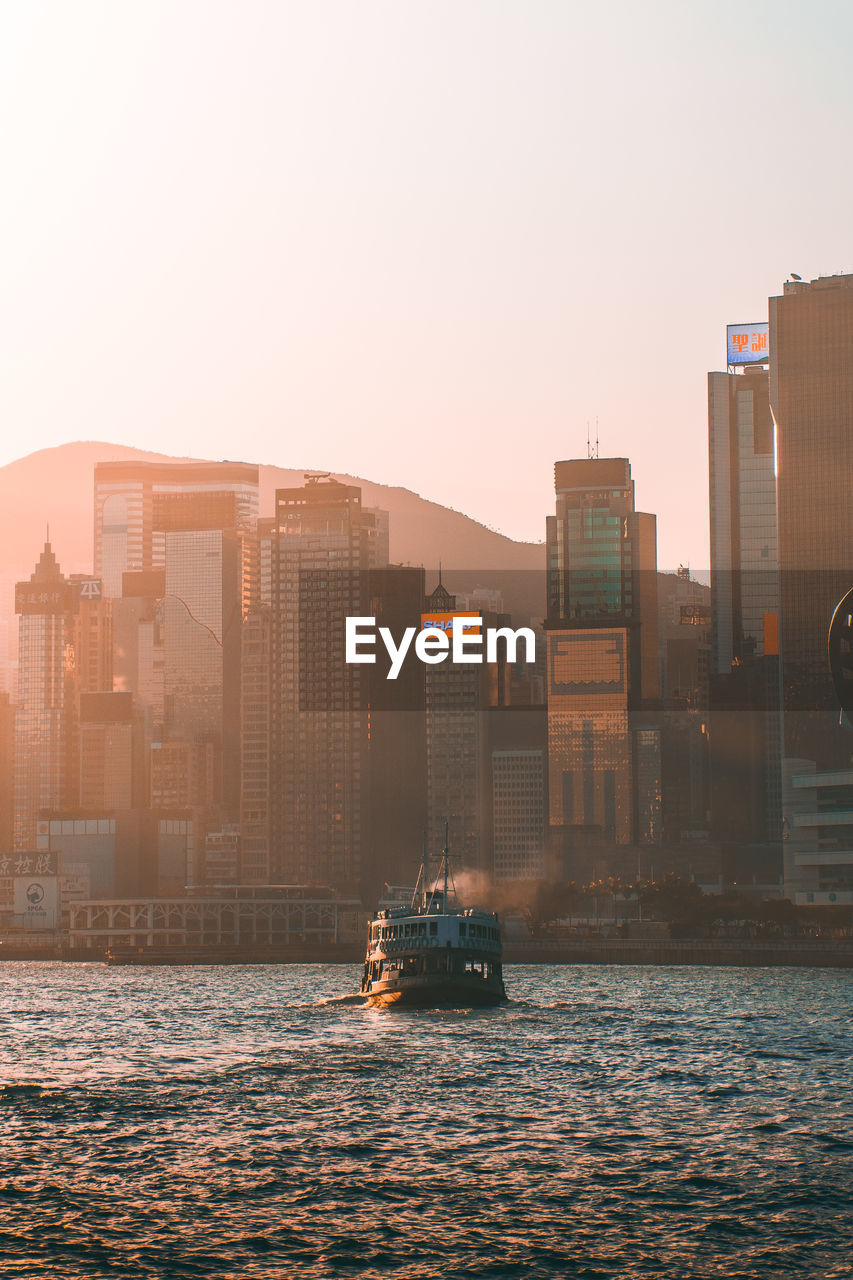 Ship in sea against buildings and clear sky during sunset