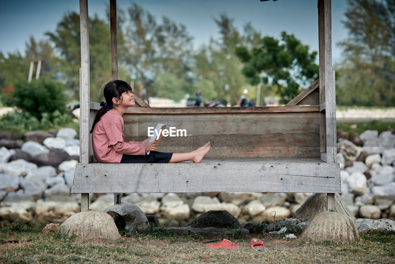 Little girl sitting and reading a book at a wooden gazebo outdoors