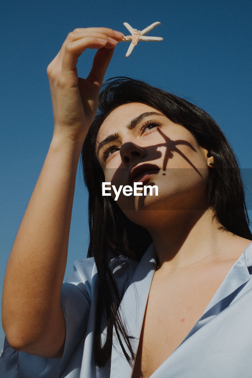 LOW ANGLE PORTRAIT OF YOUNG WOMAN AGAINST SKY