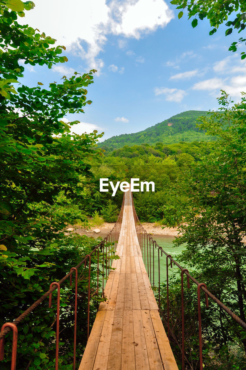 Footbridge amidst trees against sky