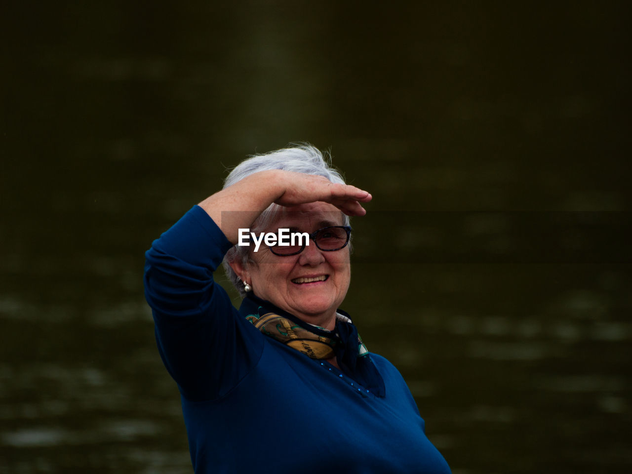 Portrait of smiling woman shielding eyes while standing against river