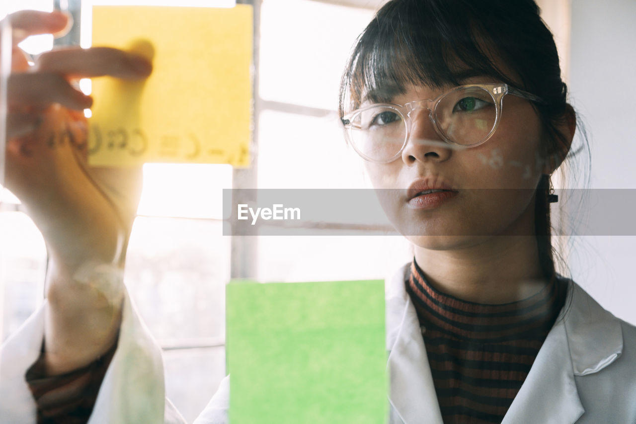 Young scientist sticking adhesive note on transparent glass