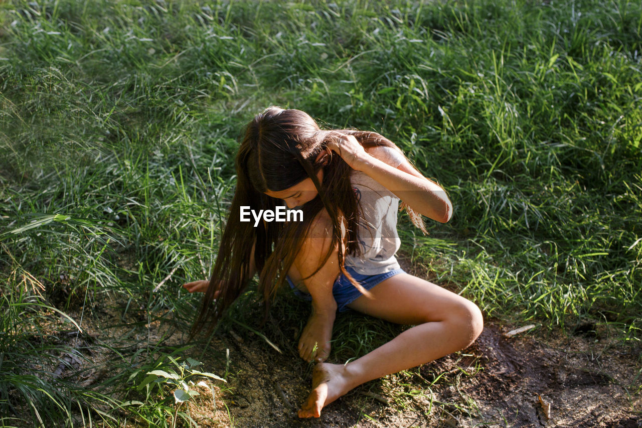 Above-view of young girl sitting in grass with muddy feet in sunshine