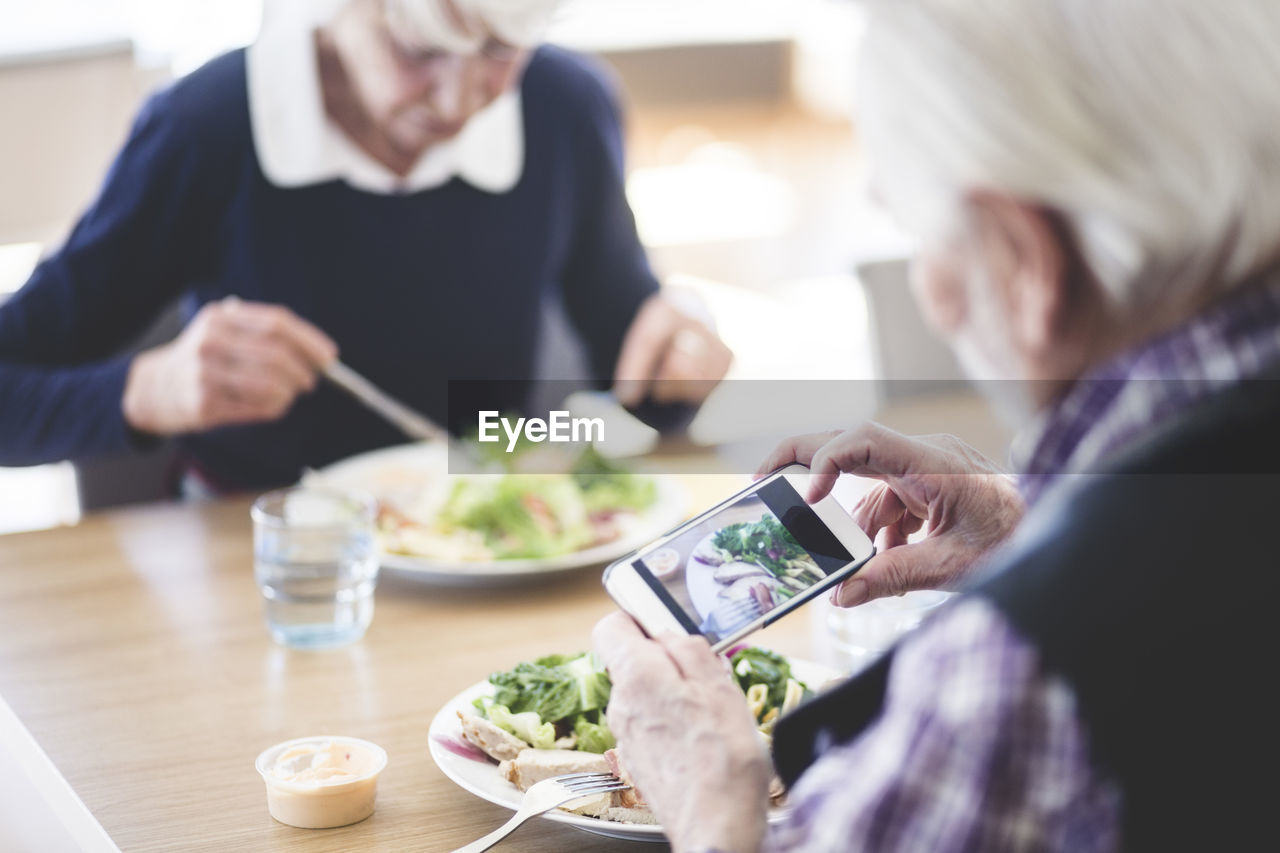 Senior man photographing food using smart phone while having lunch with woman at table