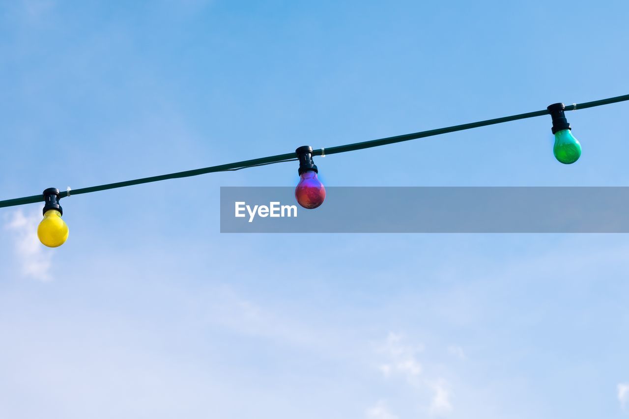 Low angle view of colorful bulbs hanging on cable against sky