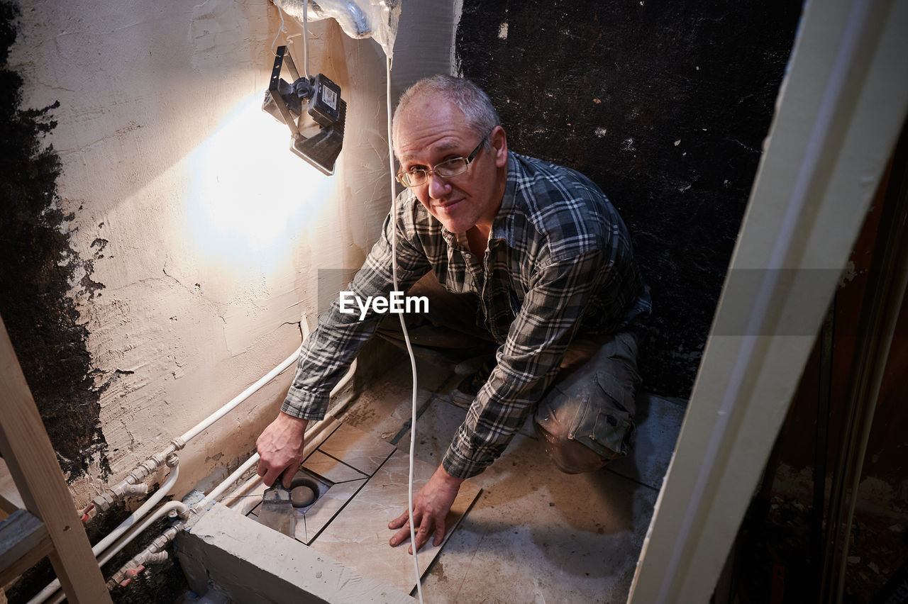 High angle portrait of man installing tiles at bathroom