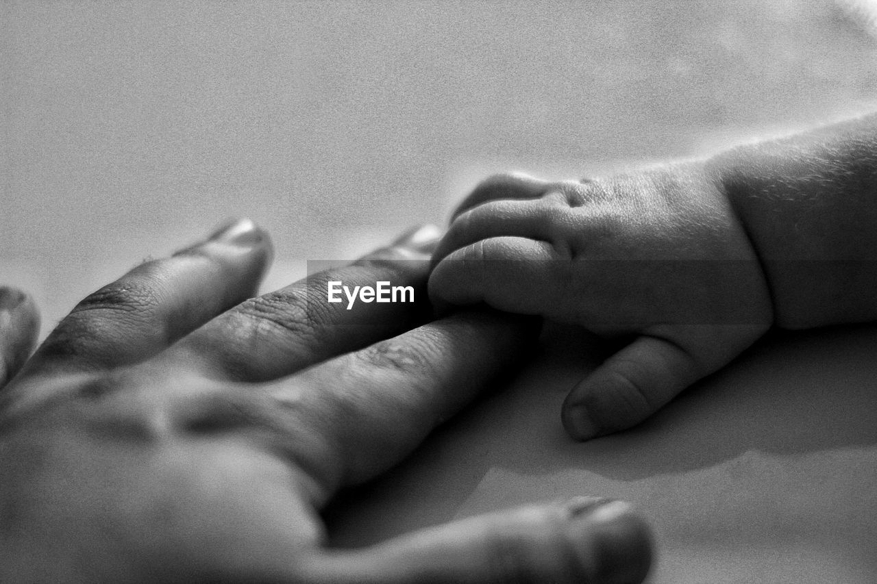 Cropped hands of parent and baby holding hands on bed