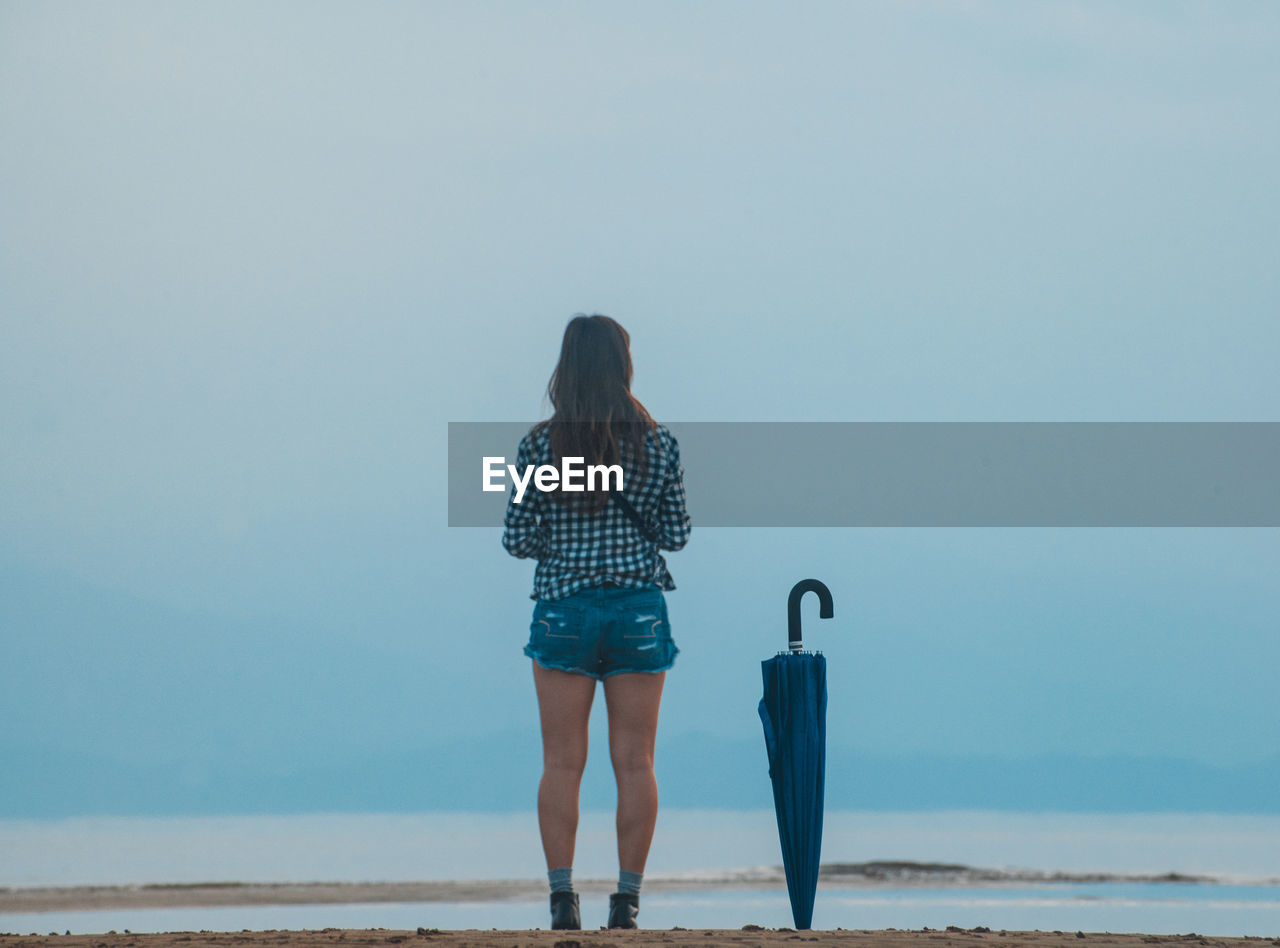 Rear view of woman with umbrella standing against blue sky 