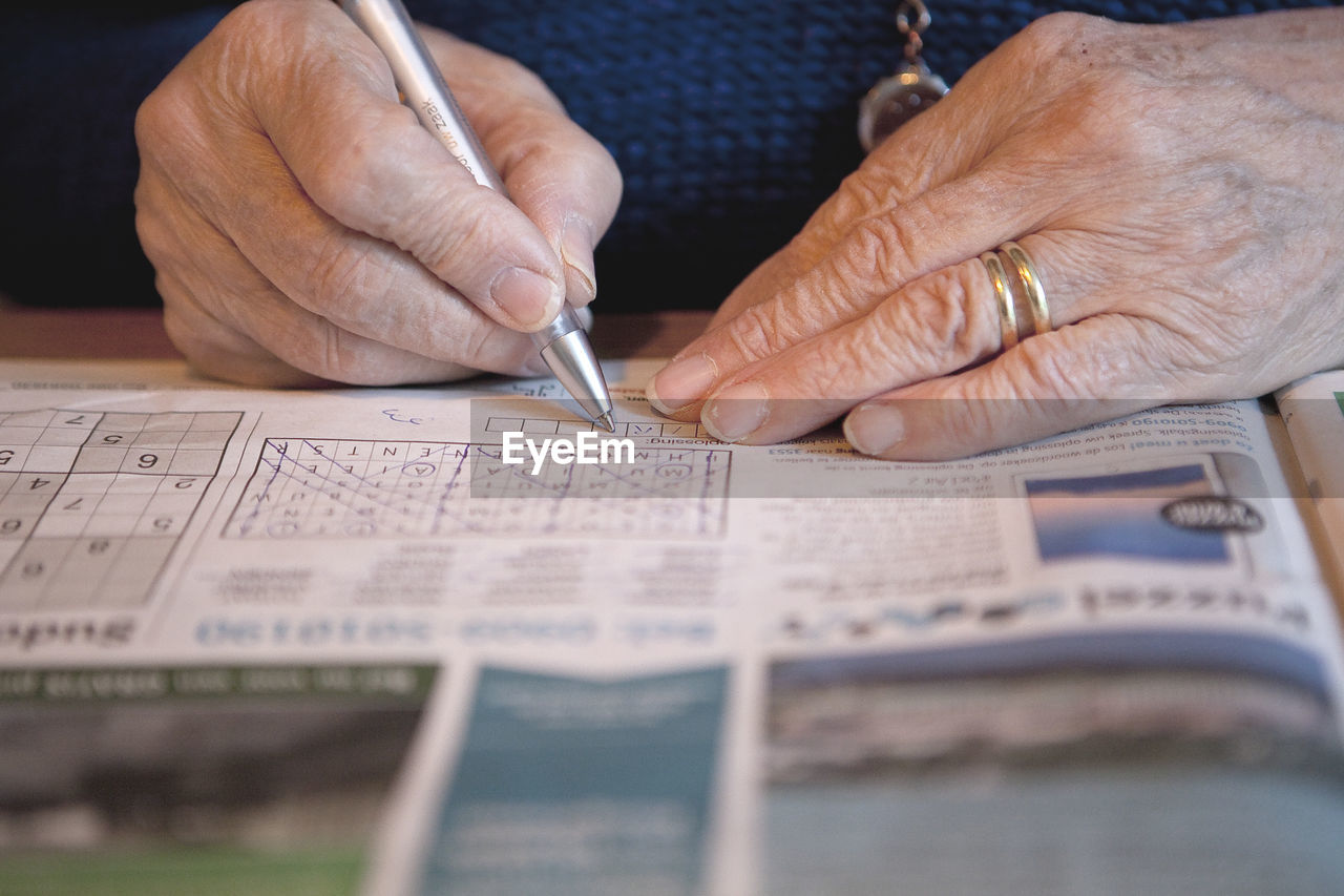 Cropped hand of senior woman writing on newspaper