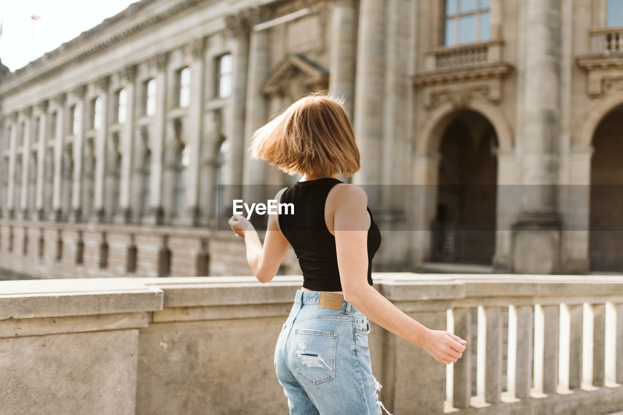 REAR VIEW OF WOMAN STANDING IN FRONT OF BUILDING