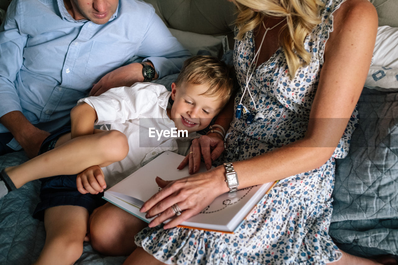 Happy young boy snuggling his parents while they read on bed