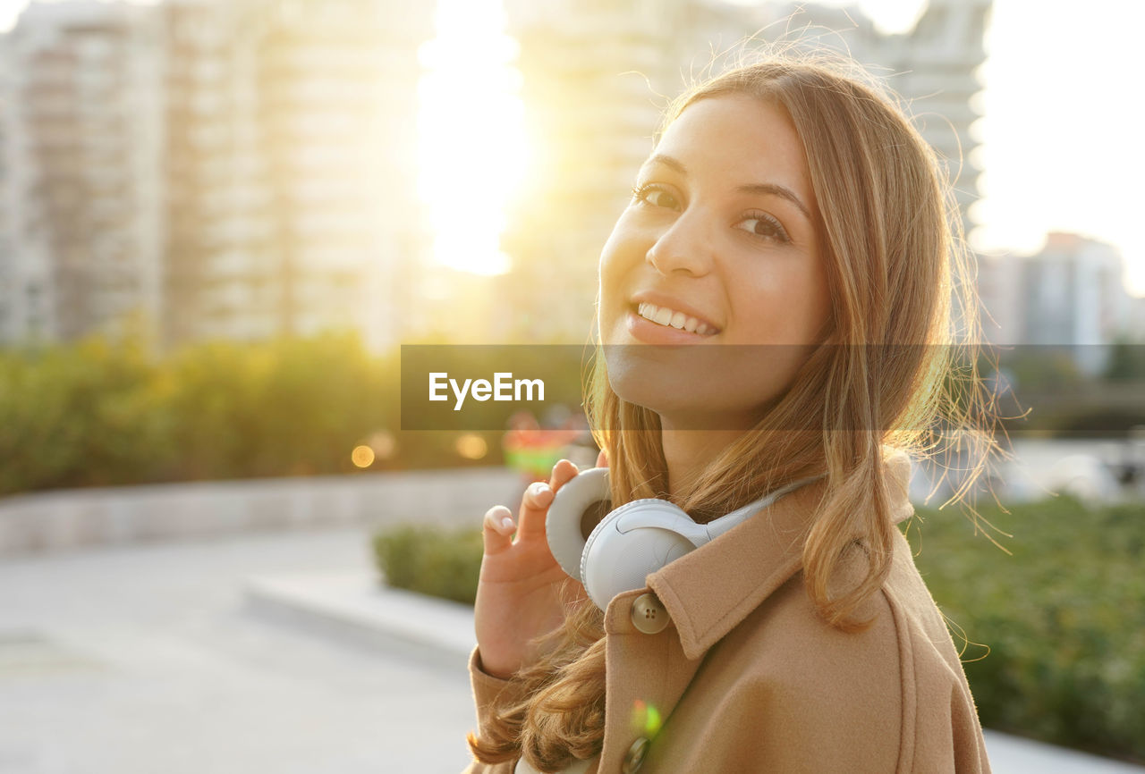 Young woman takes off her headphones and smiles on camera relaxing outdoor at sunset