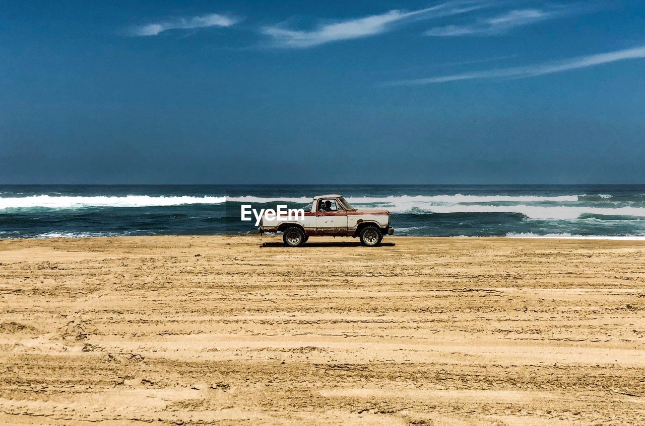 Pick-up truck moving on beach against blue sky during sunny day