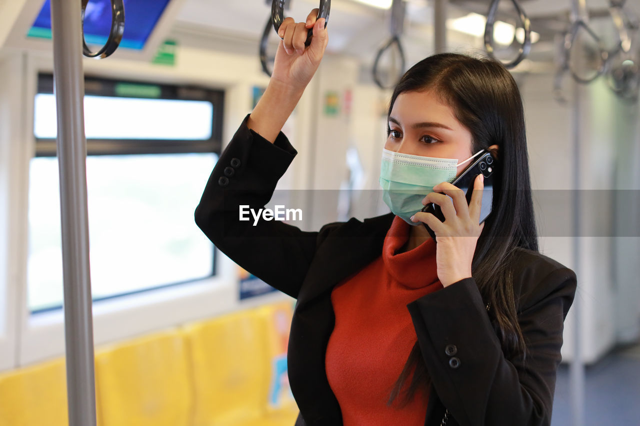 YOUNG WOMAN USING PHONE WHILE STANDING ON LAPTOP