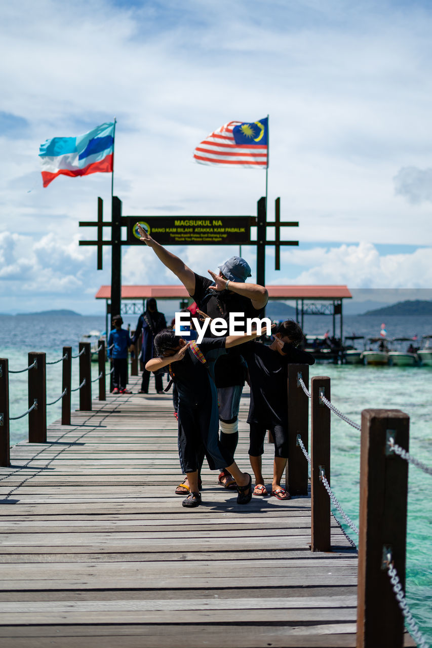 People on wooden bridge over sea against sky in bohey dulang.