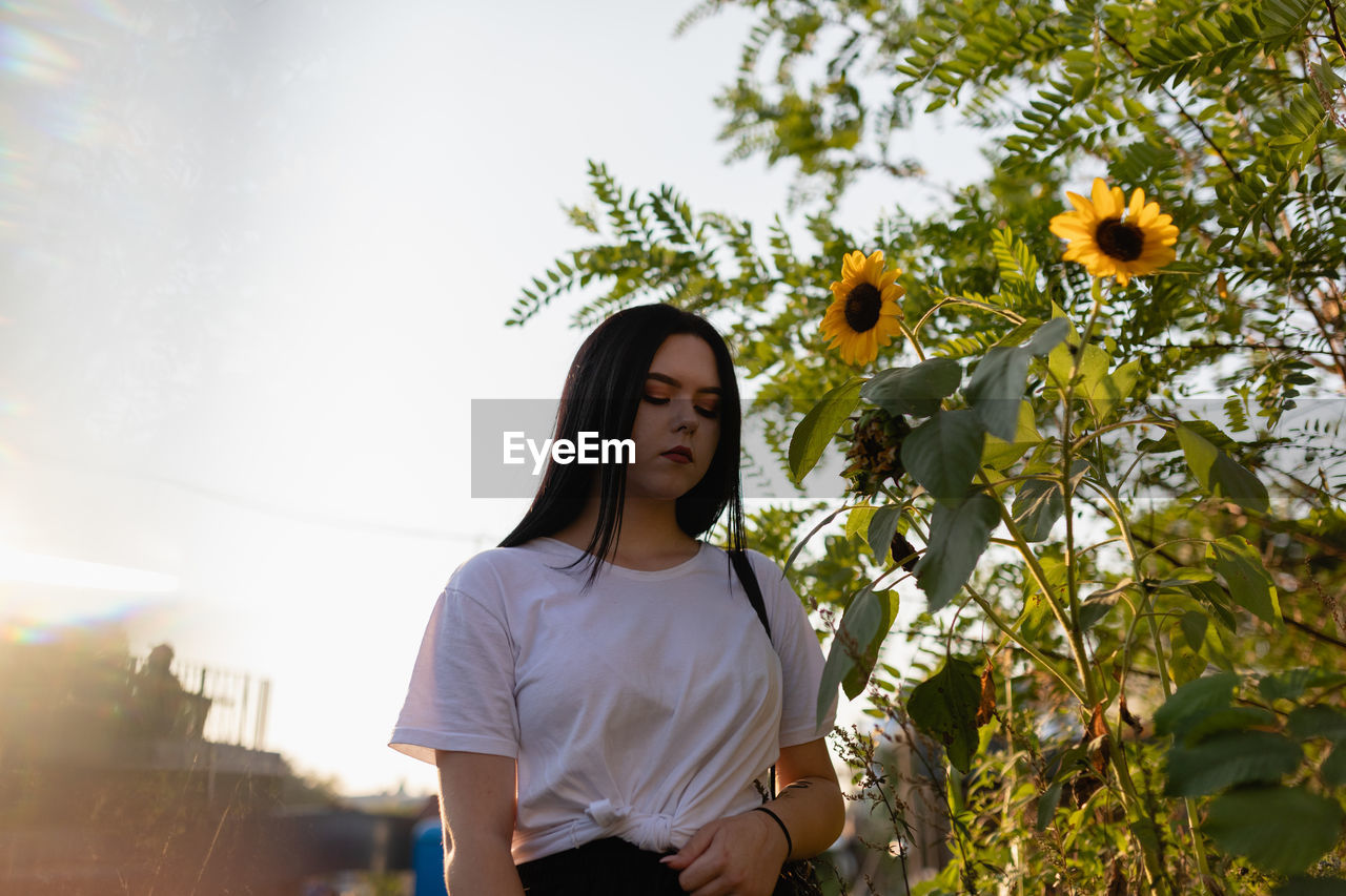 Low angle view of woman standing by flowering plant against sky