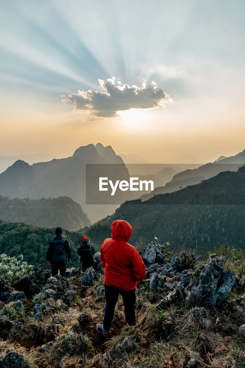 Rear view of men walking on mountain against sky during sunset