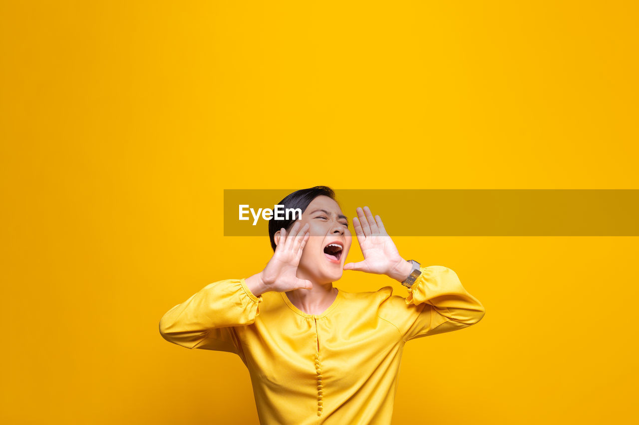 Woman shouting while standing against yellow background