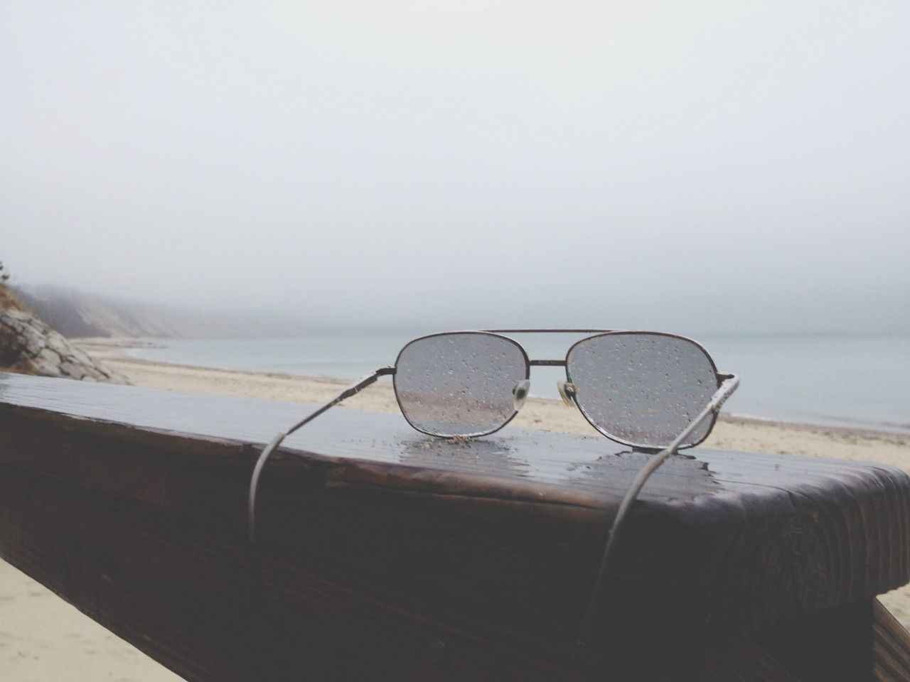 Close-up of wet sunglasses on retaining wall against cloudy sky in rain