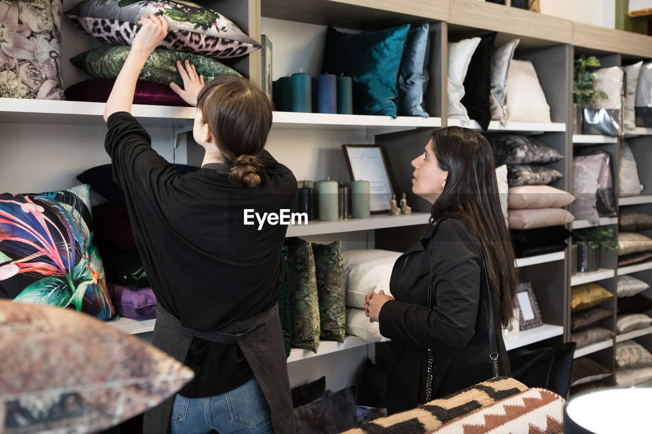 Mature female customer looking at young owner holding cushion in rack