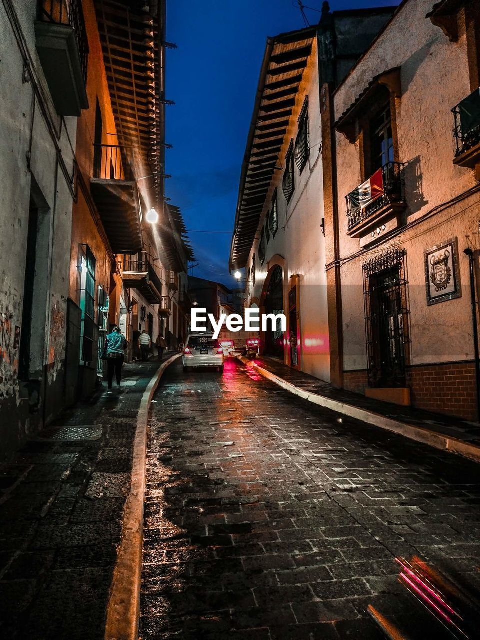 WET STREET AMIDST ILLUMINATED BUILDINGS IN CITY