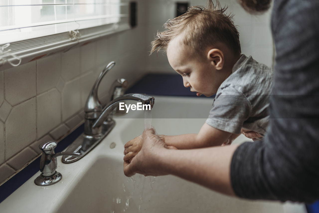 Side view of young boy having hands washed in sink by dad