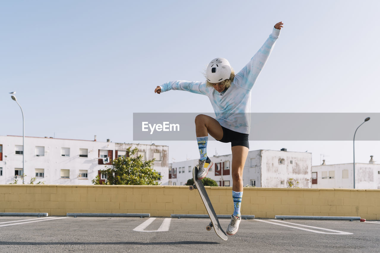 Young woman with skateboard skating on rooftop at city