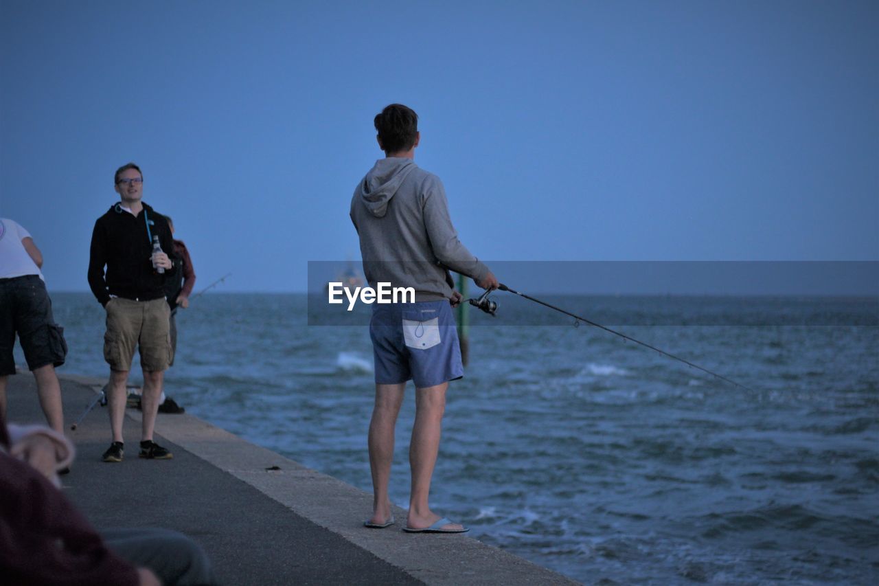 REAR VIEW OF MAN ON BEACH AGAINST CLEAR SKY