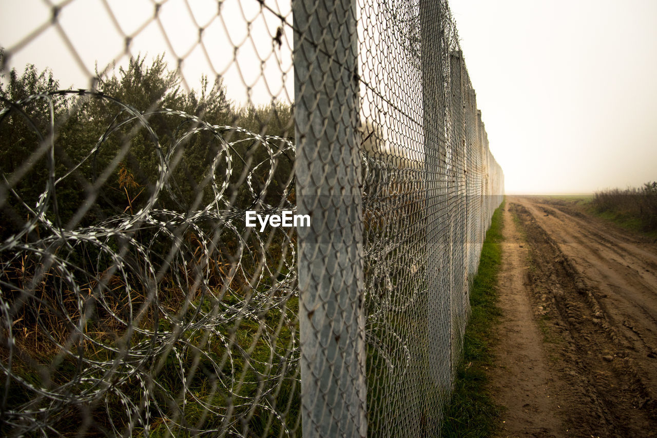 Empty dirt road by chainlink fence on field