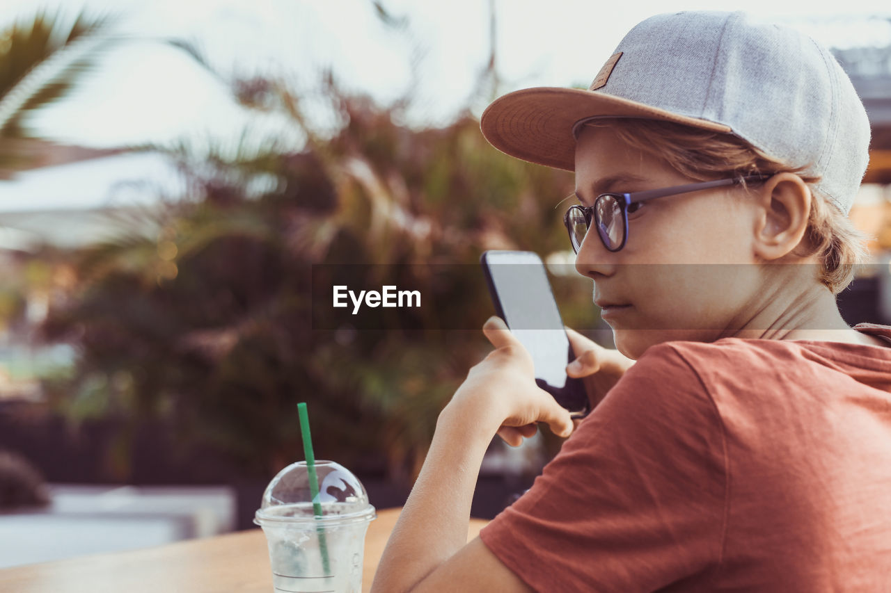 Boy using mobile phone while holding sitting outdoors