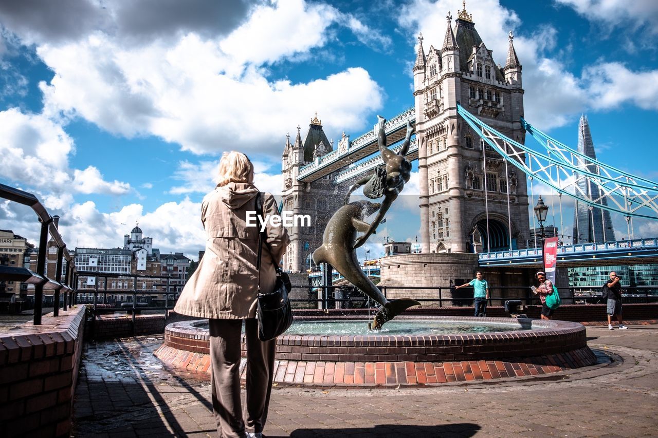 Rear view of woman watching girl and dolphin statue by london bridge