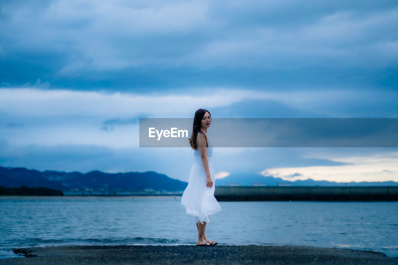 FULL LENGTH OF WOMAN STANDING IN WATER AGAINST SKY