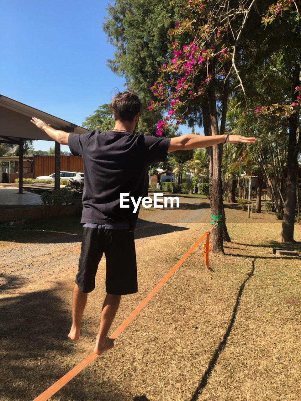 REAR VIEW OF MAN WALKING ON FOOTPATH BY TREES