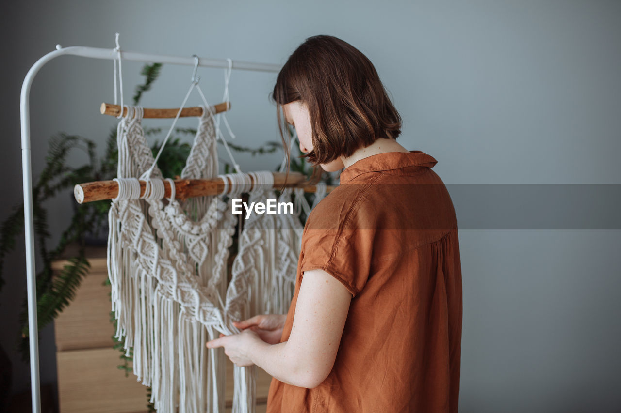 A young girl weaves macrame panels at home