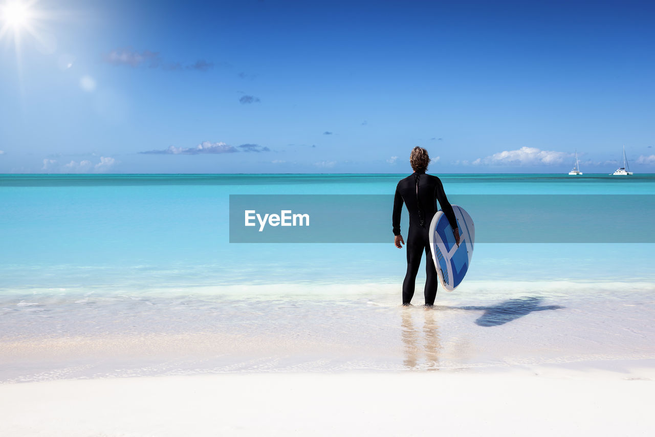 Rear view of man with surfboard standing on beach